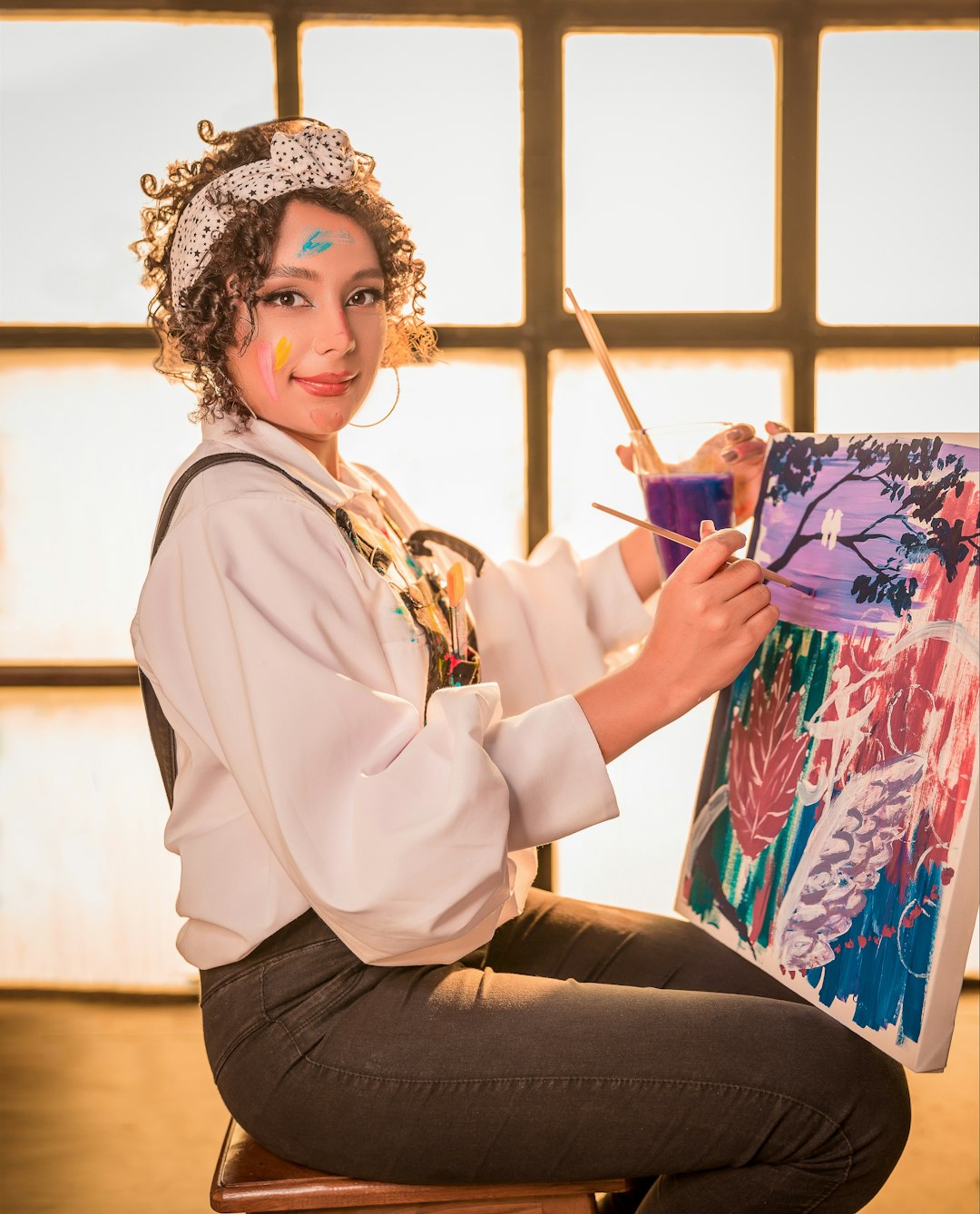 a-woman-sitting-on-a-stool-painting-with-a-brush-oemrjzbcjz8