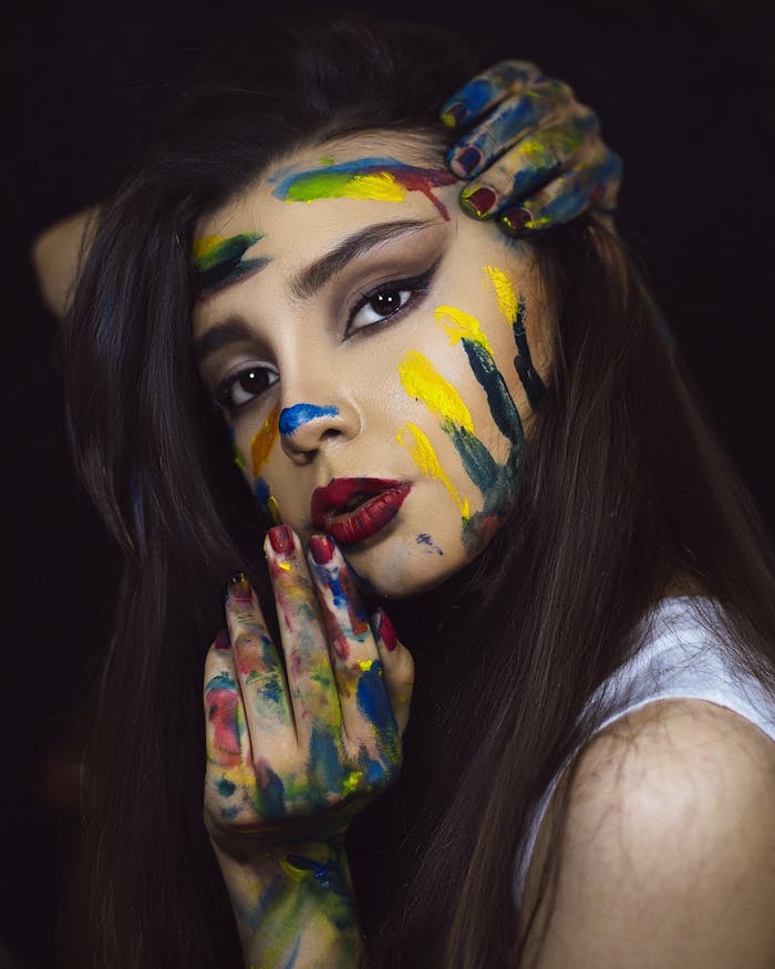 Vibrant portrait of a woman with colorful face and hand paint, capturing artistic expression.