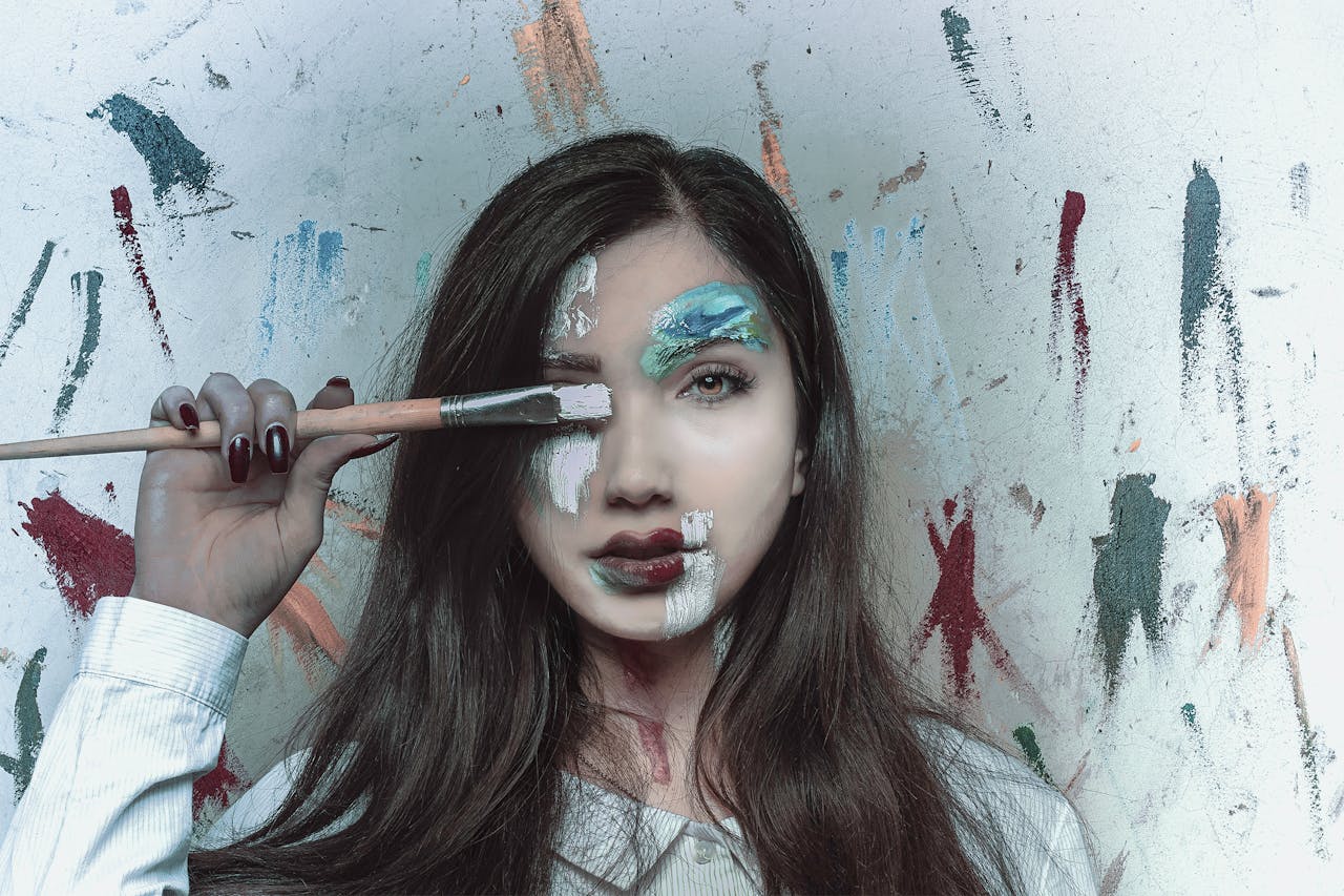 Vibrant portrait showcasing a woman with creative face paint and brush, embodying artistic expression.